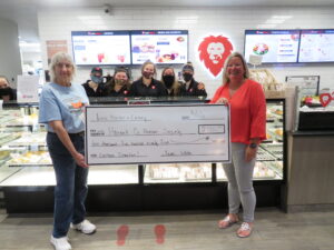 Two people pose with a large check with 5 other people in the background. 